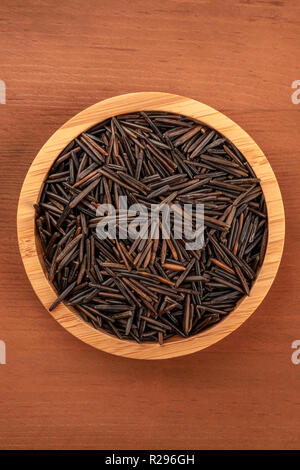 Black wild rice, shot from above in a wooden bowl on a dark rustic background with a place for text Stock Photo