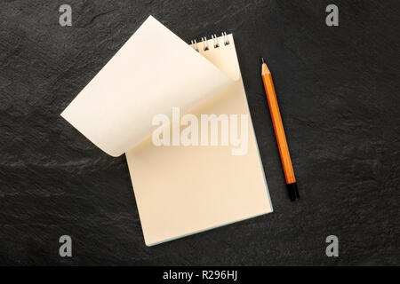 To Turn a New Page. A spiral note pad with a blank sheet of paper, shot from the top on a dark background with a sharp pencil and a place for text Stock Photo