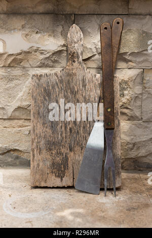 Old wooden cutting board with big wooden fork. Cooking accessories. Used cutting board. Kitchen utensils. Stock Photo