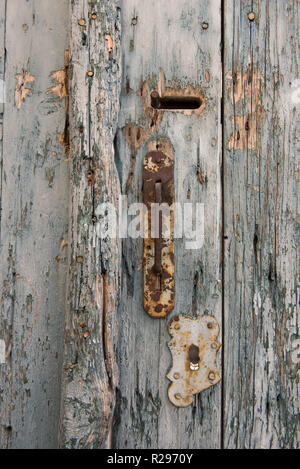Old and rusty door knob with keyhole on pale and vintage blue wooden doors. Stock Photo