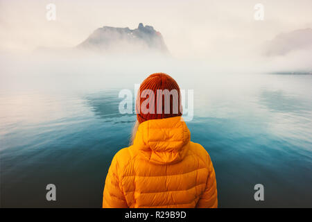 Woman alone looking at foggy cold sea traveling adventure lifestyle outdoor solitude emotions winter clothing hat and down jacket Stock Photo