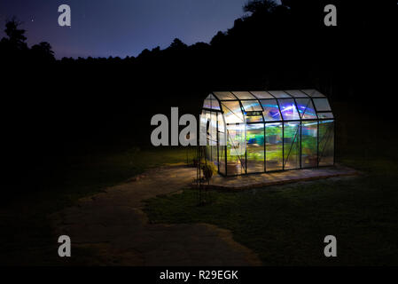 Small greenhouse with its lights on and stars behind Stock Photo