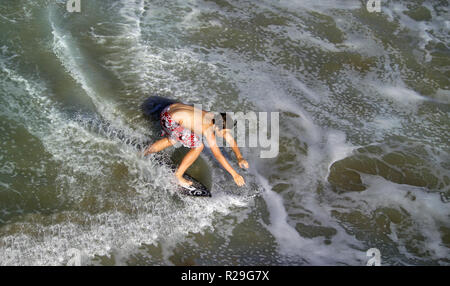 A young skimboarder keeps his balance to skim along on water that gently rolls in from the Pacific Ocean onto a sandy beach along the coast of Southern California, USA. Falls are common until a skimmer can judge the best incoming waves to ride before running toward them from the shore with his board. Stock Photo