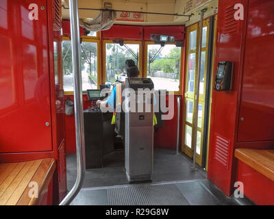 Inside a streetcar looking past the self-service ticket machine and the female driver of such historic electric vehicles that have been providing public transportation on steel rails throughout the southern city of New Orleans, Louisiana, USA, for more than a century. Twenty-five miles of track host four streetcar lines, including the iconic St. Charles line that started service in 1835 and is the oldest continuously-operating streetcar line in the world. The red car seen here travels through the heart of the city on the Canal Street line and takes about 30 minutes to ride from end to end. Stock Photo