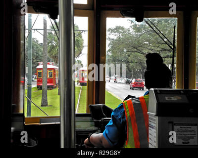 Inside a streetcar looking past the self-service ticket machine and the female driver of such historic electric vehicles that have been providing public transportation on steel rails throughout the southern city of New Orleans, Louisiana, USA, for more than a century. Twenty-five miles of track host four streetcar lines, including the iconic St. Charles line that started service in 1835 and is the oldest continuously-operating streetcar line in the world. The red cars seen here travel through the heart of the city on the Canal Street line and takes about 30 minutes to ride from end to end. Stock Photo