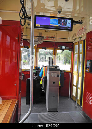Inside a streetcar looking past the self-service ticket machine and the female driver of such historic electric vehicles that have been providing public transportation on steel rails throughout the southern city of New Orleans, Louisiana, USA, for more than a century. Twenty-five miles of track host four streetcar lines, including the iconic St. Charles line that started service in 1835 and is the oldest continuously-operating streetcar line in the world. The red car seen here travels through the heart of the city on the Canal Street line and takes about 30 minutes to ride from end to end. Stock Photo