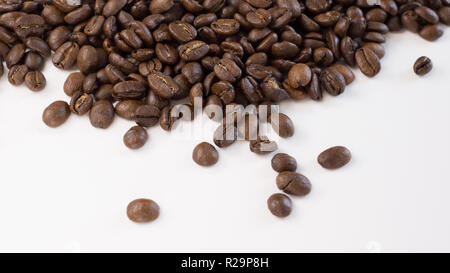 Brown, roasted coffee beans are shown up close and loosely spread out on a plain, white surface. Stock Photo