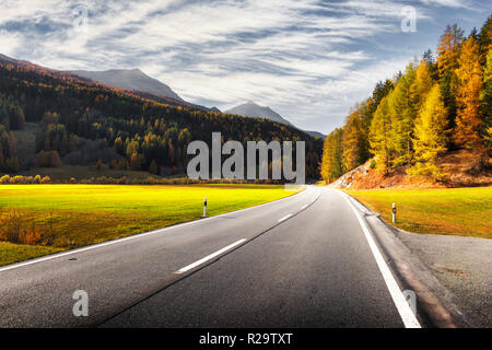 Amazing view of alpine road, orange larch forest and high mountains on background. Switzerland, near Italy border. Landscape photography Stock Photo