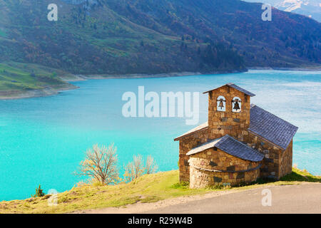 Sunny picturesque view of stone chapel on Roselend lake (Lac de Roselend) in France Alps (Auvergne-Rhone-Alpes). Landscape photography