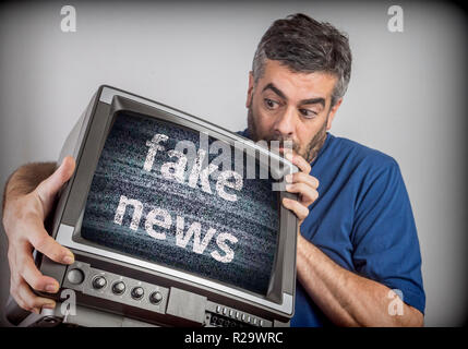 Middle-aged man holds a TV with fake news screen, conceptual image Stock Photo