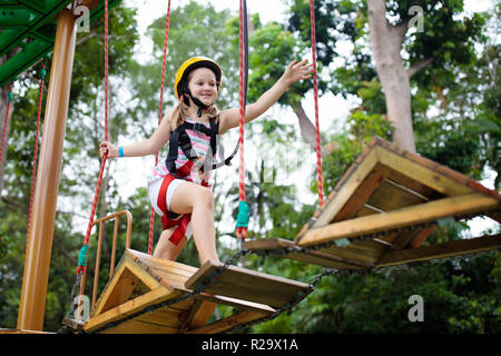 Child in forest adventure park. Kids climb on high rope trail. Agility and climbing outdoor amusement center for children. Little girl playing outdoor