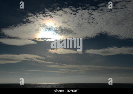 a rainbow of heavenly light shines through the high altitude thin cirrus clouds over the sea Stock Photo