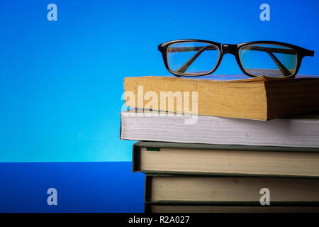 EDUCATION CONCEPT with stack of old book and reading glasses on a blue background. Stock Photo