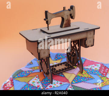 Mini sewing machine, made of wood, on a patchwork rug, with yellow background. Stock Photo