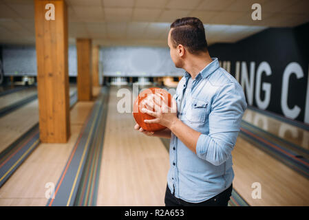 Male bowler standing on lane and poses with ball in hands, back view. Bowling alley player prepares to throw strike shot in club, active leisure Stock Photo