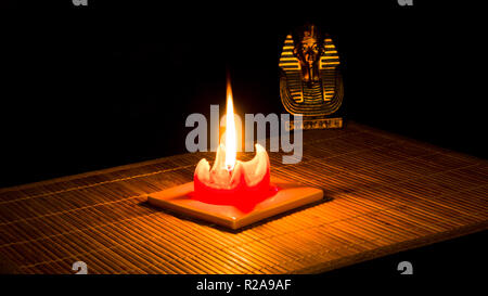 Statue of Tutankhamun lit by a candle on bamboo mat on a black background. Stock Photo