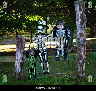three boys in skeleton halloween costumes hanging on an old wrought iron gate Stock Photo