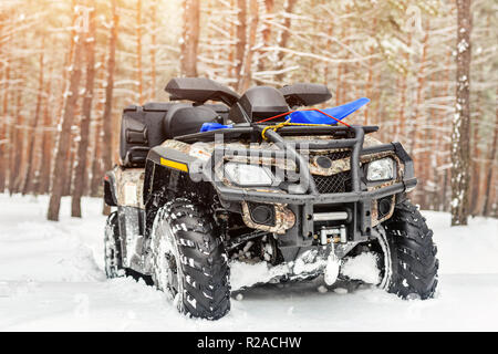 Close-up ATV 4wd quad bike in forest at winter. 4wd all-terreain vehicle stand in heavy snow with deep wheel track. Seasonal extreme sport adventure and trip. Copyspace Stock Photo