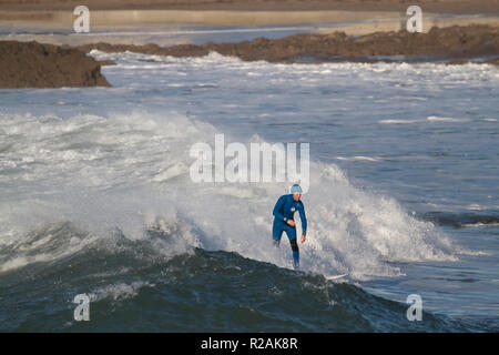 Cornwall, UK. 18th Nov 2018. A Surfer rides the huge waves in Bude,Cornwall as people make the most of the glorious sunshine and walk along the beach while walking their dogs.Credit:Keith Larby/Alamy Live News Stock Photo