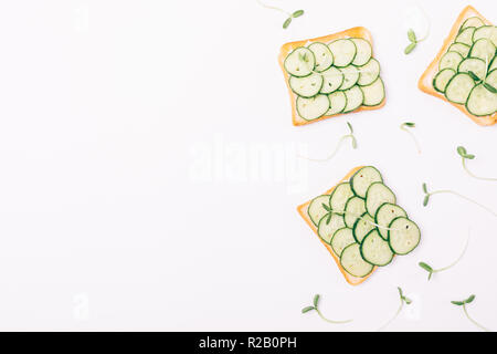Flat lay decorative side frame of toasts with fresh cucumbers and green seed sprouts on white background, top view with copy space. Stock Photo