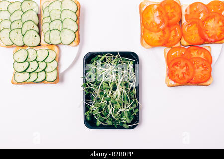 Two types of sandwiches with cucumbers and tomatoes next to box of sprouted sunflower seeds, top view. Stock Photo