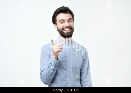 Happy positive bearded hispanic man dressed in blue shirt pointing his index finger upwards Stock Photo