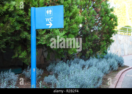 Blue pointer direction to the toilet on the background of natural plants, flowers, trees with green leaves in the park. Background Stock Photo