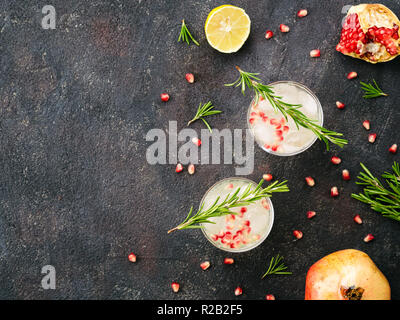 Autumn and winter cocktails idea - white sangria with rosemary, pomegrante and lemon juice and ingredients on black cement background. Copy space. Top view or flat-lay. Stock Photo