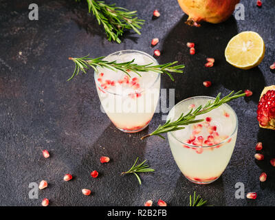Autumn and winter cocktails idea - white sangria with rosemary, pomegrante and lemon juice and ingredients on black cement background. Copy space. Stock Photo