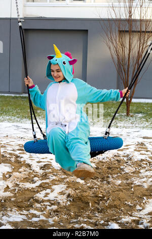 cute woman in kigurumi unicorn costume joying swing on the street Stock Photo