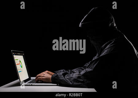 A male hacker cover his head with the hood trying to steal the data from a laptop computer Stock Photo