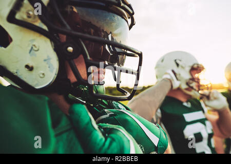 Closeup of a young American football player wearing a helmet and visor standing with his teammates during a practice session Stock Photo