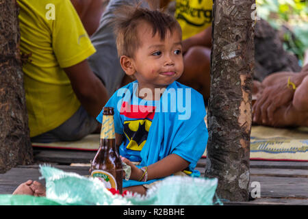 Don Khone, Laos - April 24, 2018: Funny child sitting next to a beer bottle in a remote village of Laos Stock Photo