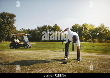 Sporty senior man placing a golf ball on a tee while standing on a golf course on a sunny day Stock Photo