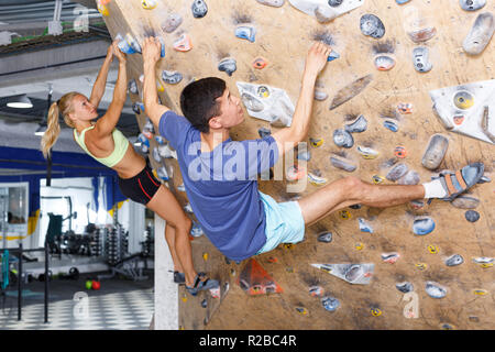 Woman and man alpinists practicing in pair indoor rock-climbing on climbing wall Stock Photo