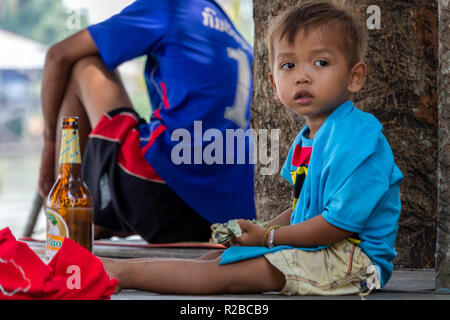 Don Khone, Laos - April 24, 2018: Local kid holding money in his hands and sitting next to a beer bottle Stock Photo