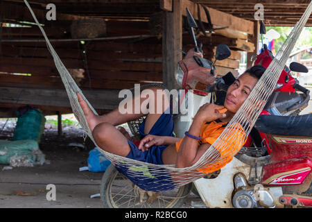 Don Khone, Laos - April 24, 2018: Young lao man resting in a hammock in front of a wooden house Stock Photo