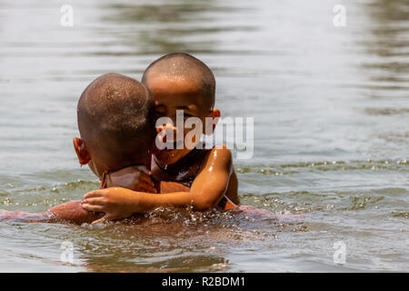 Don Khone, Laos - April 24, 2018: Local kids holding each other and swimming in the Mekong river Stock Photo