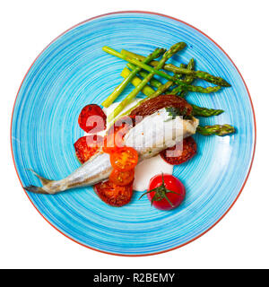 Top view of baked whiting served on blue plate with sun-dried tomatoes, sparrowgrass and garlic creamy sauce. Isolated over white background Stock Photo