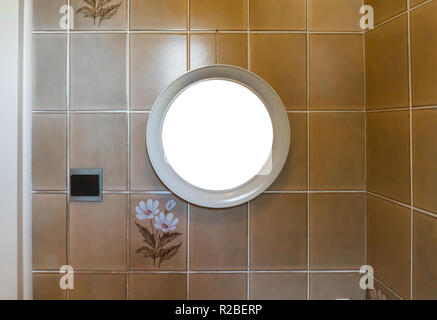 empty blank round mirror frame hanging in the bathroom on a tiled wall decorated with flowers Stock Photo