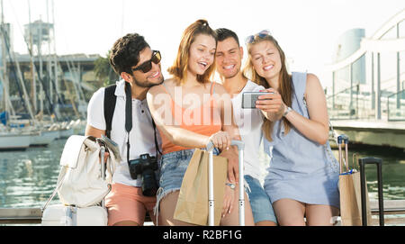 group travellers taking selfie on camera in smartphone on waterfront in town on summer day Stock Photo