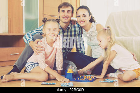 Happy smiling young parents with two little daughters playing at lotto at home Stock Photo