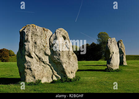 Aircraft vapour trails criss-crossing a cloudless blue sky over part of the Avebury stone circle. Stock Photo