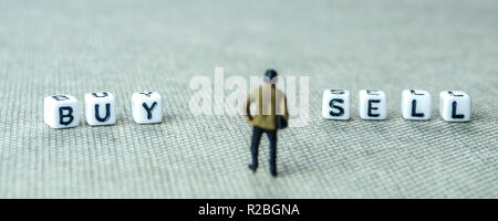 closeup of miniature figurines of businessman standing in front of white dices with sell and buy words written on them Stock Photo