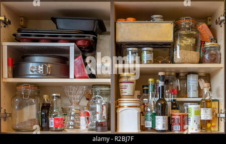 Domestic kitchen cupboards interior with stored ingredients, baking tins, coffee jugs, and food. Stock Photo