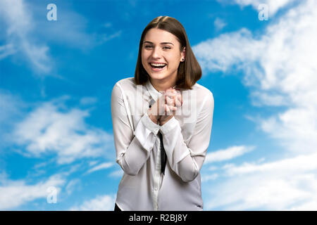 Laughing woman on cloudy sky background. Young happy female is laughing heartily outrdoor. Human expression of happiness. Stock Photo