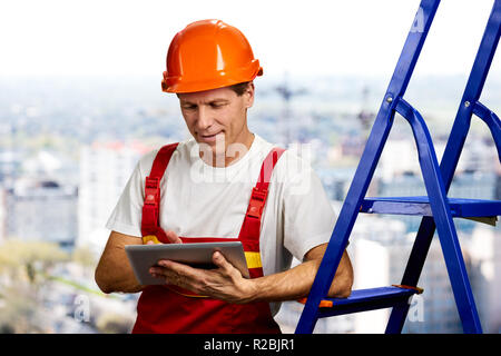 Smiling engineer using digital tablet. Mature contractor in hardhat working on computer tablet on blurred background. Checking new object. Stock Photo