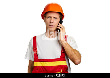 Portrait of builder talking on phone. Angry construction engineer talking on smartphone over white background. Stock Photo