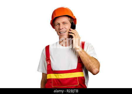 Cheerful builder talking on cell phone. Smiling construction worker with smartphone over white background and copy space. Stock Photo