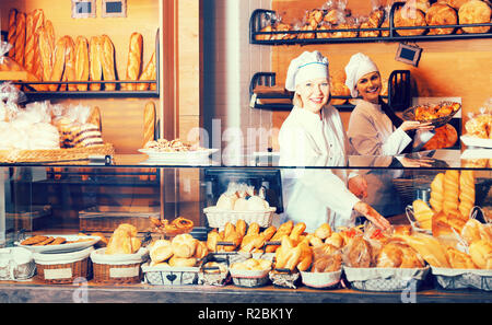 Two smiling women selling bread and different pastry in bakery Stock Photo
